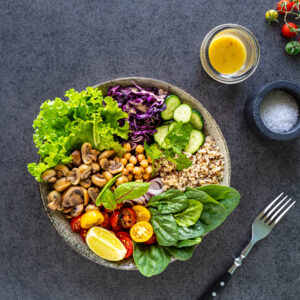 Quinoa, mushrooms, lettuce, red cabbage, spinach, cucumbers, tomatoes, a bowl of Buddha on a dark background, top view. Delicious balanced nutrition concept